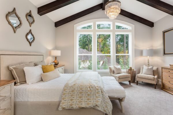 master-bedroom-in-new-luxury-home-with-chandelier-and-large-bank-of-windows-with-view-of-trees-1222623844-212940f4f89e4b69b6ce56fd968e9351-min